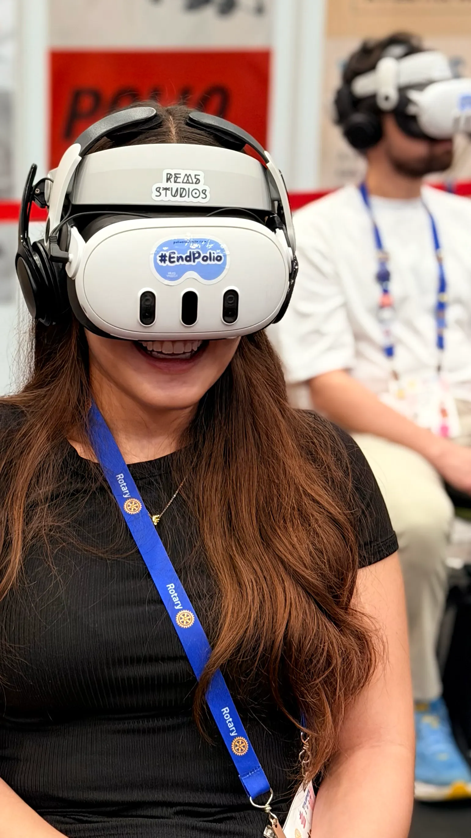 A smiling Rotary 2026 attendee wearing a Rotary lanyard and a VR headset marked #EndPolio, mid-experience at the booth