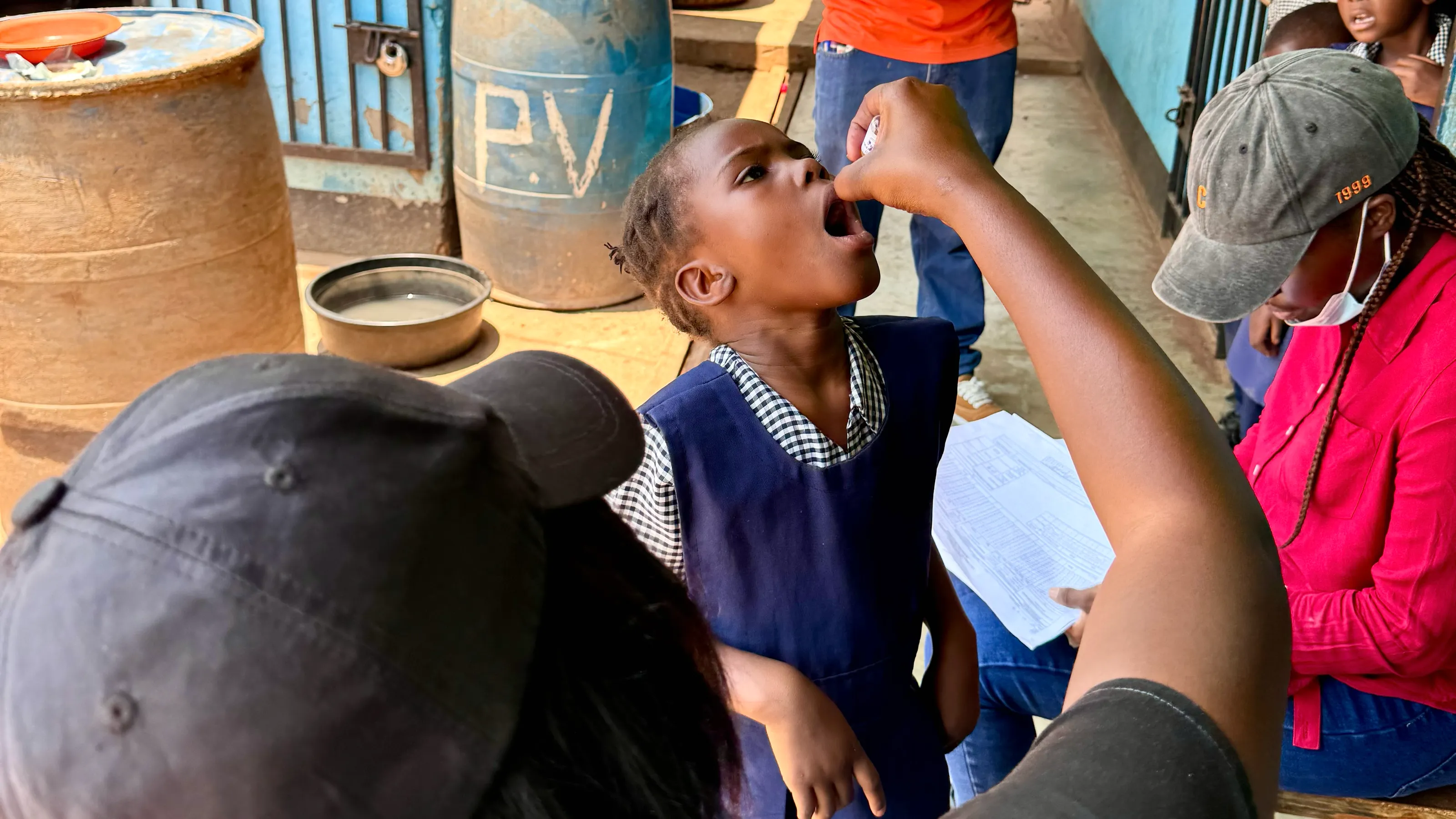 A frame from Polio’s Last Mile: a health worker gives a young girl two drops of oral polio vaccine during a door-to-door campaign